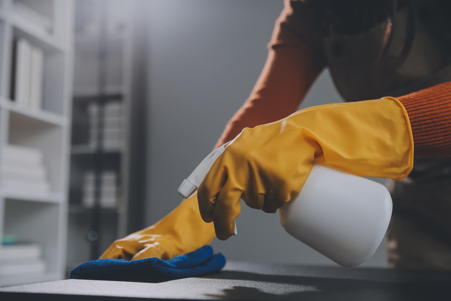 Cleaner sanitising an office desk with a microfibre cloth